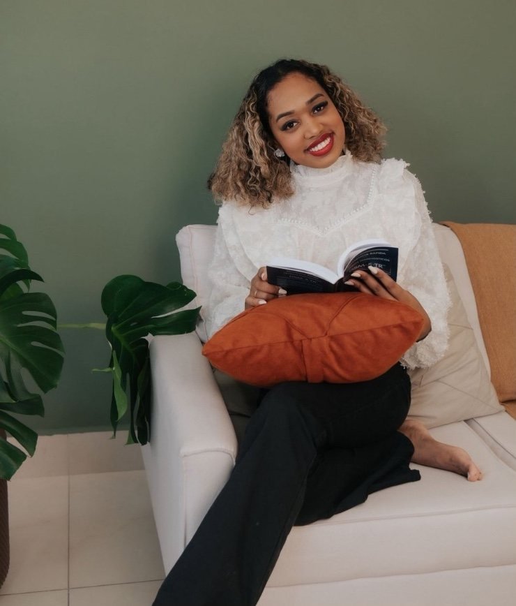 Gabriela Luiza, psicóloga e neuropsicóloga, sentada no sofá com um livro